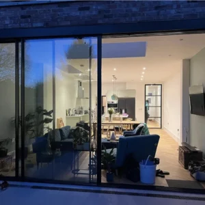 Black aluminium sliding doors at night, London garden extension